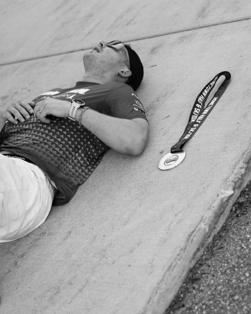 Male marathon runner fatigued laying on ground next to medal
