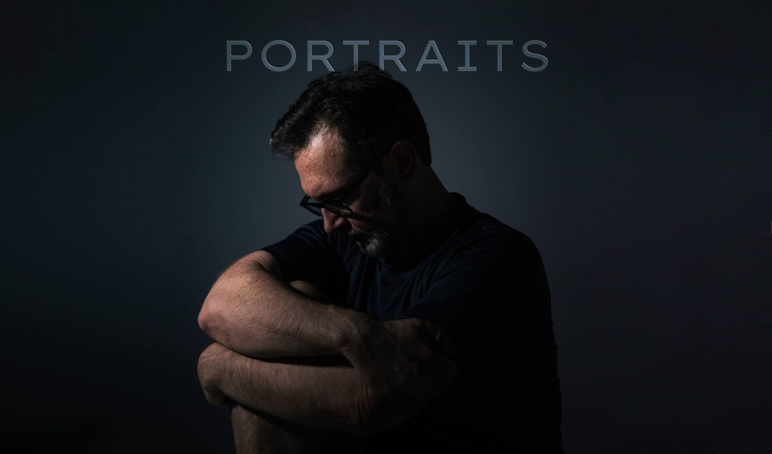 Dark Portrait man hugging knee while looking down, lighting from left upper
